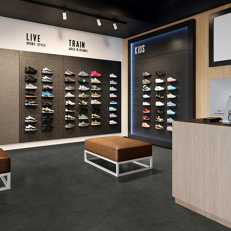 Sneaker-Store mit Schuhwänden, Sitzbänken und Kassenbereich auf recyceltem Elastikboden in dunkler Steinoptik mit dezent wolkiger Struktur.
