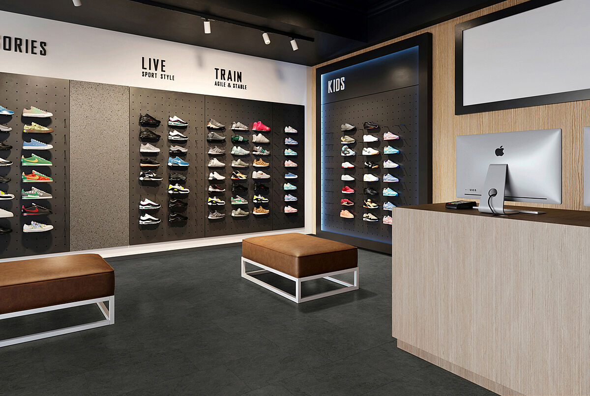 Sneaker-Store mit Schuhwänden, Sitzbänken und Kassenbereich auf recyceltem Elastikboden in dunkler Steinoptik mit dezent wolkiger Struktur.