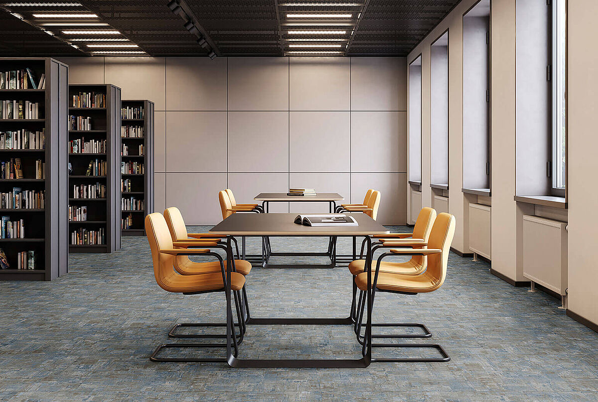 Leseraum mit Bücherregalen, Tischen und gelben Stühlen auf recyceltem Elastikboden in blau-grauer, melierter Fliesenoptik.