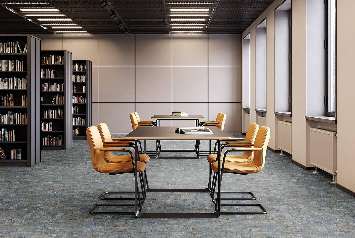 Leseraum mit Bücherregalen, Tischen und gelben Stühlen auf recyceltem Elastikboden in blau-grauer, melierter Fliesenoptik.