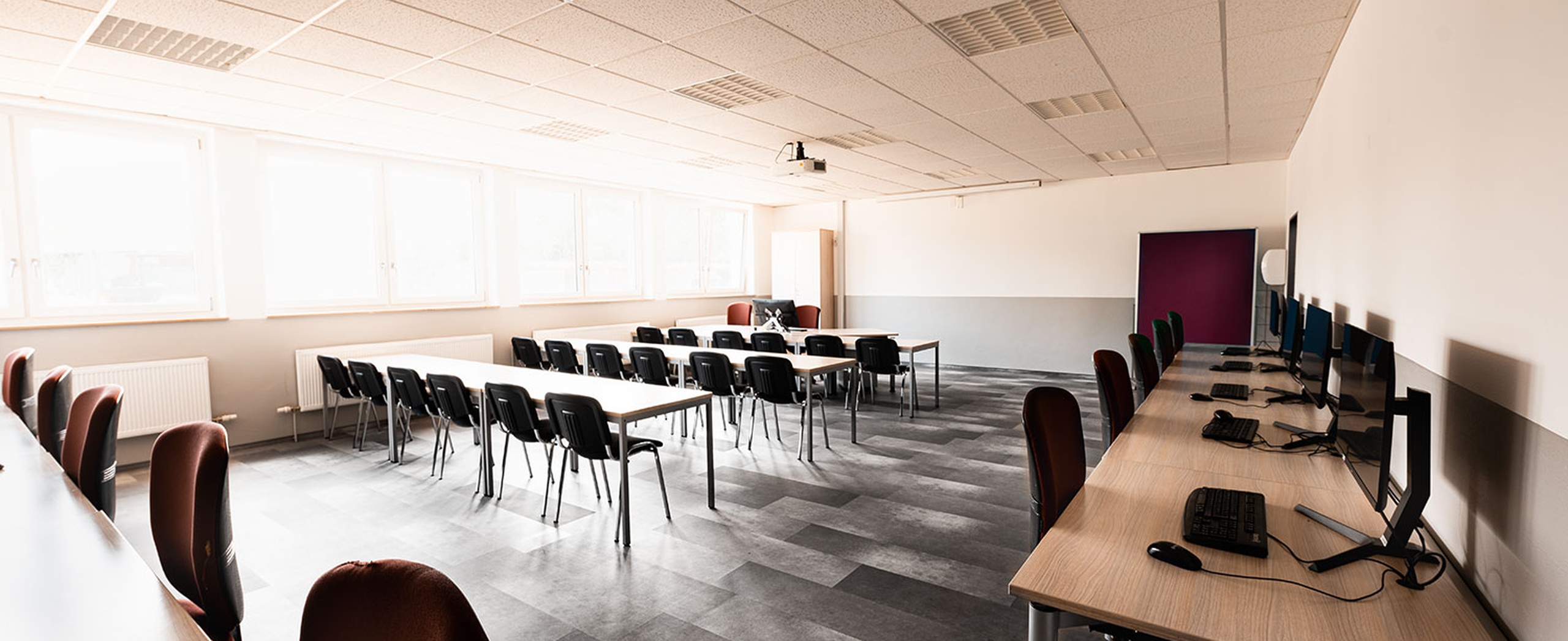 Heller Schulungsraum mit elastischem, recyceltem Bodenbelag in Schieferoptik – strapazierfähig, pflegeleicht und ideal für Bildungs- und Arbeitsbereiche mit hoher Nutzung. Heller Schulungsraum mit elastischem recyceltem Bodenbelag in Schieferoptik, Tischen, Stühlen und Computerarbeitsplätzen.